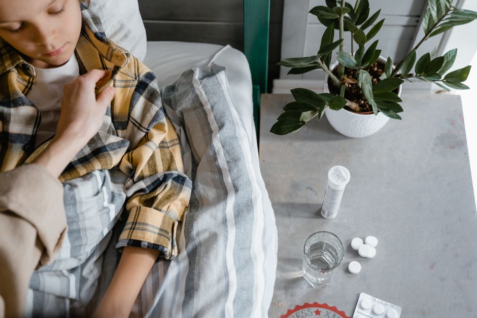 A comforting hand tends to a sick child resting in bed beside a table with medical supplies.